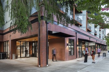 Corner exterior with trees, balconies, and people outside retail spaces
